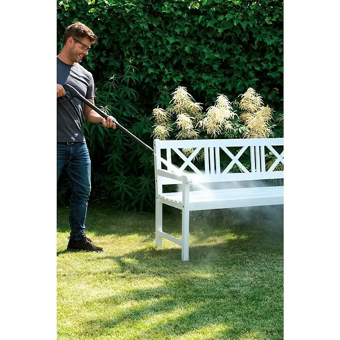 Nilfisk Hidrolimpiadora de alta presión CORE 150 PC - 150 bar, 2.000 W, Capacidad de bombeo: 468 l/h - Un hombre limpia un banco de jardín blanco con una hidrolavadora. El dispositivo elimina la suciedad de manera eficaz, garantizando la limpieza en exteriores.