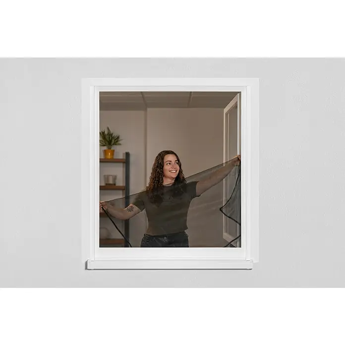 Schellenberg Mosquitera Easy Open - An x Al: 130 x 150 cm, Montaje de la mosquitera: Enganche, Color bastidor: Antracita - Una mujer sujeta una mosquitera negra a un marco de ventana blanca, diseñada para mantener los insectos fuera permitiendo el flujo de aire.