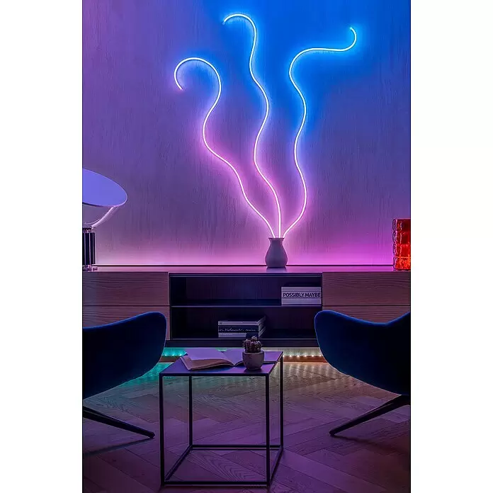 Twinkly Tira de luces LED Flex - Largo: 2 m, Color de luz: RGB, 15 W - Obra de arte de neón con líneas onduladas rosas y azules que surgen de un jarrón, sobre un mueble de madera en un salón moderno.