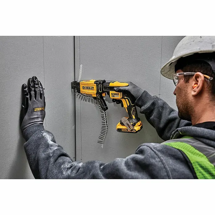 DeWalt Atornillador para placas de yeso de batería DCF620D2-QW - 18 V, 2 baterías, 2 Ah, 30 Nm - Un trabajador de la construcción usa un atornillador de tablaroca DeWalt amarillo para fijar un panel a la pared, enfatizando la herramienta y su función.