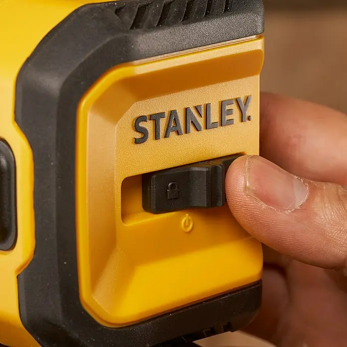 Stanley Nivel láser en cruz STHT77611-0 - Zona de trabajo máx.: 10 m - Primer plano de un dispositivo de medición láser amarillo de Stanley accionado por una mano que acciona el mecanismo de bloqueo.