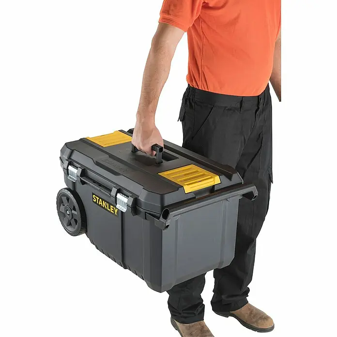 Stanley Caja para herramientas STST1-80150 - L x An x Al: 34,4 x 66,5 x 40,4 cm, Polipropileno, Capacidad volumétrica: 50 l - Una persona lleva una caja de herramientas Stanley negra y amarilla con ruedas. La caja de herramientas es el foco principal.