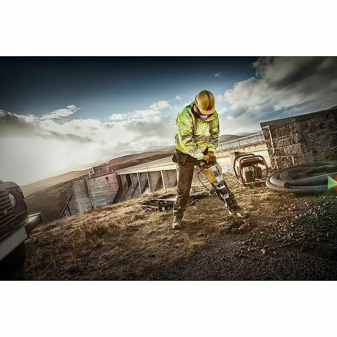 DeWalt Martillo perforador D25902K - 1.550 W, 19 J, Alojamiento SDS-MAX - Un trabajador de la construcción utilizando un martillo neumático en una presa, destacando la potencia del martillo de demolición.