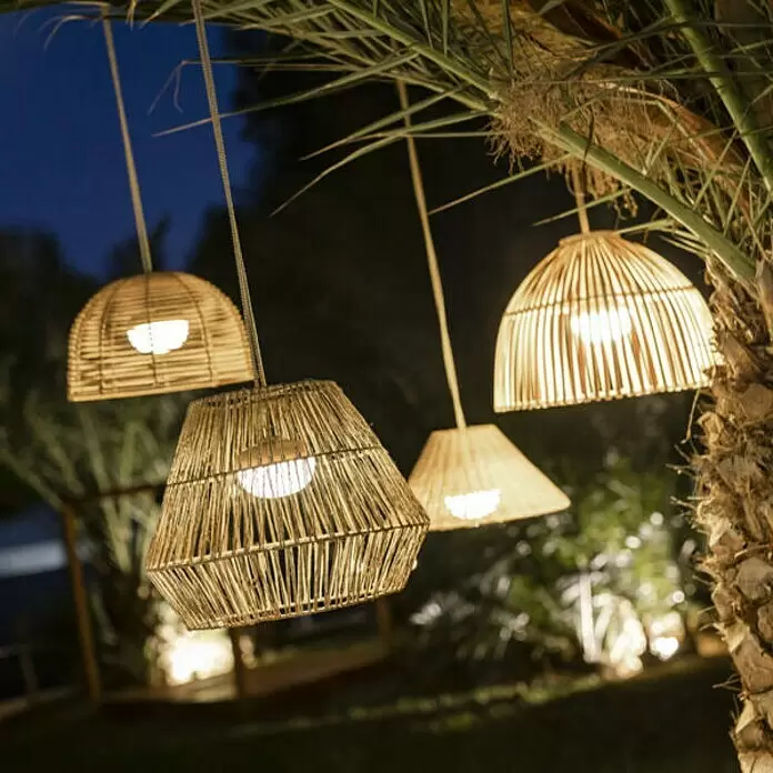 New Garden Sisine Lámpara colgante redonda batería - 9 W, Marrón, Ø x Al: 30,5 x 40 cm - Lámparas colgantes de mimbre natural iluminadas, suspendidas de una palmera, que proporcionan luz cálida en una escena nocturna exterior.