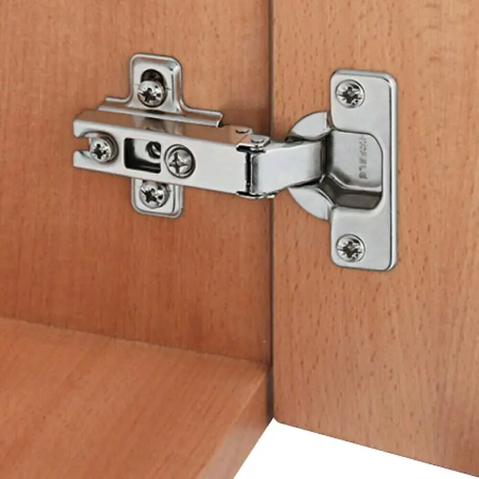Stabilit Bisagra de cazoleta - Tope medio, Diámetro cazoleta: 35 mm, Ángulo de apertura: 110 °, Cierre automático - Detalle de una bisagra Haefele plateada en una puerta de madera, destacando los detalles y la construcción de la bisagra.
