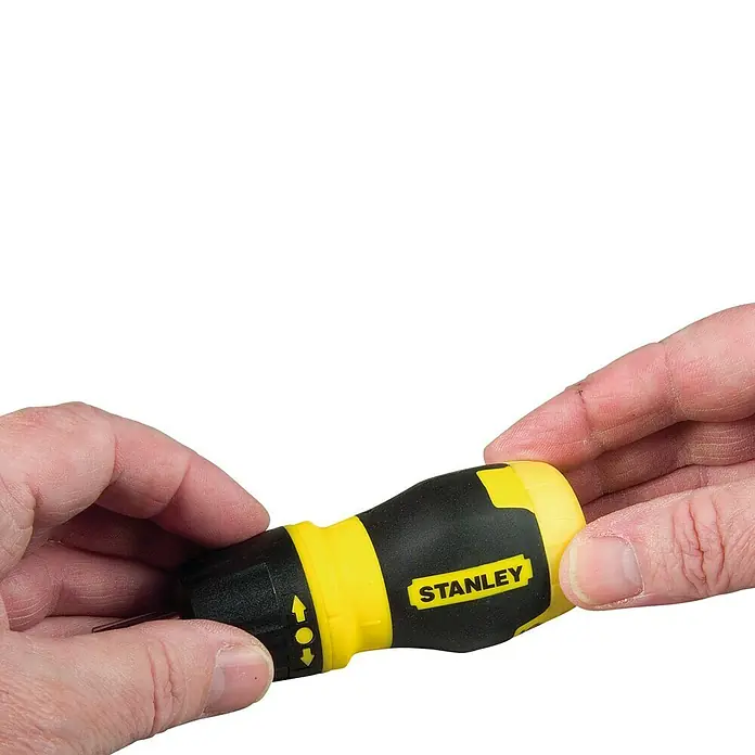 Stanley Destornillador Stubby - 7 pzs. - Primer plano de un destornillador Stanley sostenido por dos manos. La herramienta es de color amarillo y negro.