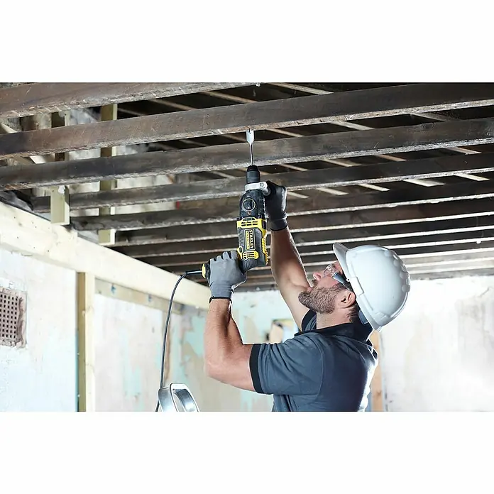 Stanley FatMax Schlagbohrmaschine FMEH1100K-QS - 1.100 W, Schnellspannbohrfutter - Mann mit Helm bohrt mit einer gelben Stanley-Bohrmaschine in eine Holzdecke.