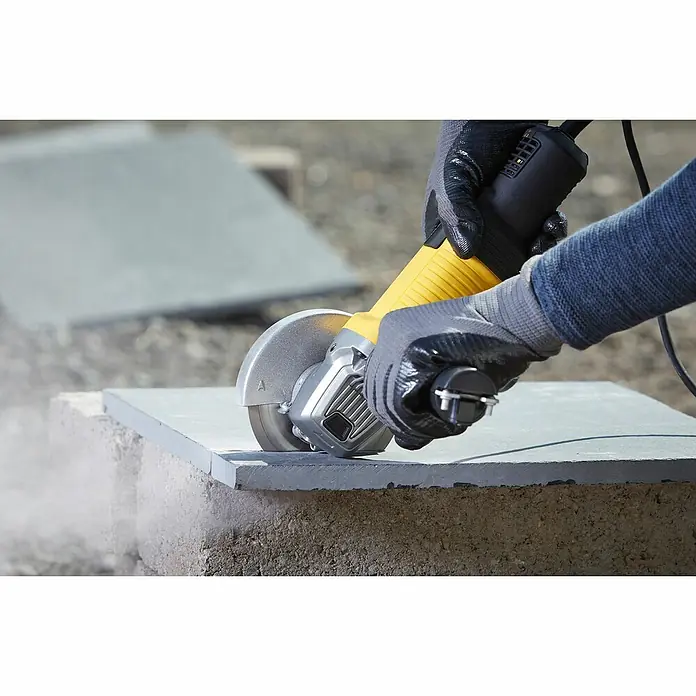 Stanley FatMax Elektro-Winkelschleifer FMEG220-QS - 850 W, 125 mm, 12.000 U/min - Nahaufnahme einer Person, die mit einer gelben und schwarzen Trennschleifmaschine einen Stein schneidet, wobei Schutzhandschuhe getragen werden.