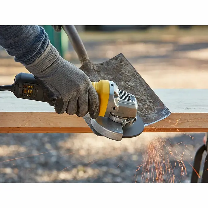 Stanley FatMax Elektro-Winkelschleifer FMEG220-QS - 850 W, 125 mm, 12.000 U/min - Nahaufnahme einer Person, die mit einem Winkelschleifer eine Schaufel schärft, wobei Funken entstehen. Der gelbe Winkelschleifer wird mit Handschuhen bedient.