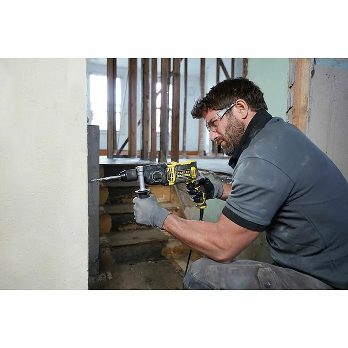Stanley FatMax Schlagbohrmaschine FMEH1100K-QS1.100 W, Schnellspannbohrfutter - Ein Bauarbeiter benutzt eine Stanley Fatmax Bohrmaschine an einer Baustelle. Das Gerät ist gelb und schwarz und scheint leistungsstark zu sein.