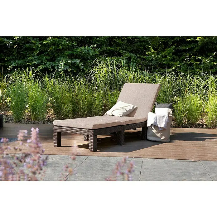 Allibert Tumbona de jardín Daytona II - Marrón, Plástico, Respaldo regulable - Una elegante tumbona marrón con cojines sobre una terraza de madera, rodeada de exuberante vegetación. Ideal para relajarse al aire libre.