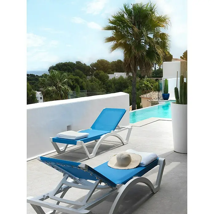 Tumbona de jardín Mykonos - 74 x 190 x 36 cm, Azul, Plástico, Respaldo regulable - Dos tumbonas azules en una terraza con piscina y palmeras al fondo. Relajación pura en un ambiente elegante.