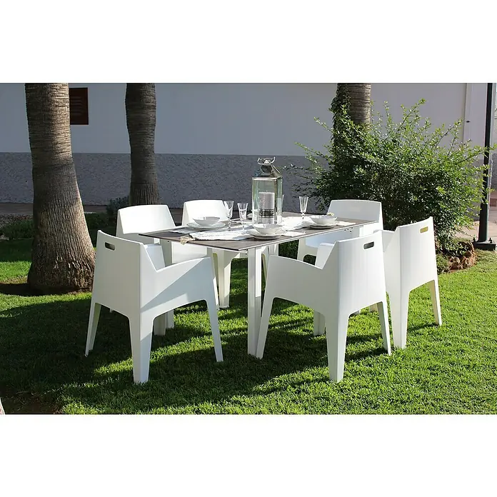 Silla de jardín Master - 60 x 67 x 82 cm, Blanco, Polipropileno, Apilable - Imagen de una mesa de comedor con seis sillas blancas en un jardín. El conjunto de exterior ofrece espacio para comidas acogedoras al aire libre.