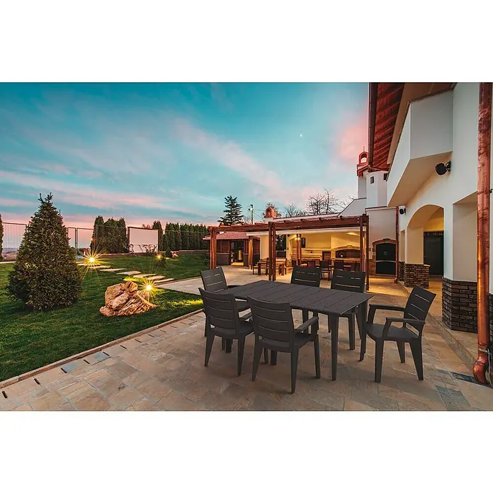 Silla de jardín Legno - Marrón, Polipropileno, Apilable, 60 x 59 x 87 cm - Un juego de mesa de jardín de plástico oscuro se encuentra en un patio rodeado de un césped cuidado con un cielo de noche.