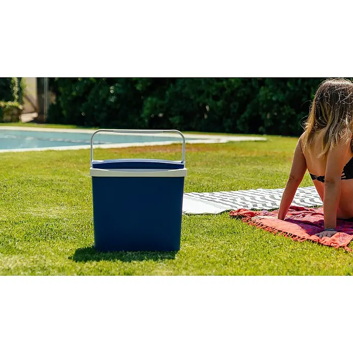 Nevera portátil - Polipropileno, 24 l - Una nevera portátil azul con asa reposa en un césped junto a una mujer sobre una toalla, ideal para picnics al aire libre.