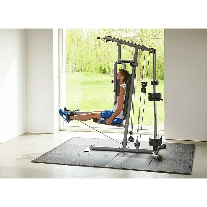 Mottez Estera antideslizante ensamblable B516VPRO - Negro, L x An: 62 x 62 cm - Hombre entrenando en un multi gimnasio. El multi gimnasio permite un entrenamiento integral de todo el cuerpo en la comodidad de tu propia casa.