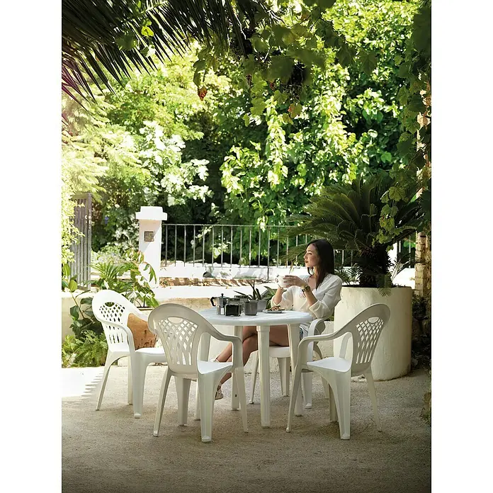 Silla de jardín Cancún - 59 x 54 x 86 cm, Blanco, Polipropileno, Apilable - Imagen de una mujer sentada en una mesa de jardín con cuatro sillas de plástico blancas, bebiendo café.