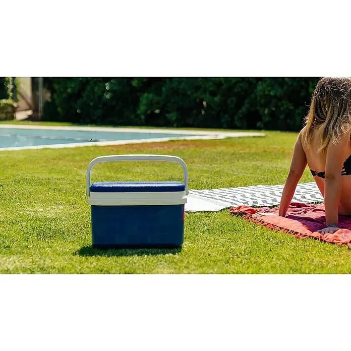Nevera portátil - Polipropileno, 16 l - Una nevera azul está sobre el césped junto a una mujer en una toalla de playa, perfecto para mantener bebidas y aperitivos fríos al aire libre.