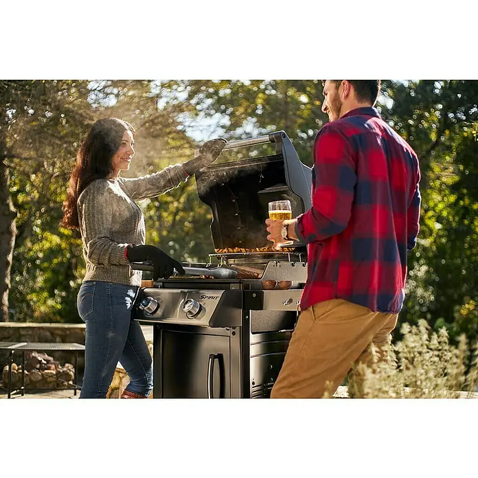 Weber Barbacoa de gas Spirit E-215 GBS - Superficie de la parrilla (An x Pr): 52 x 45 cm, Número de quemadores: 2 - Una pareja cocinando a la parrilla con una barbacoa de gas Weber Spirit. La parrilla tiene una gran superficie de cocción y es ideal para familias.