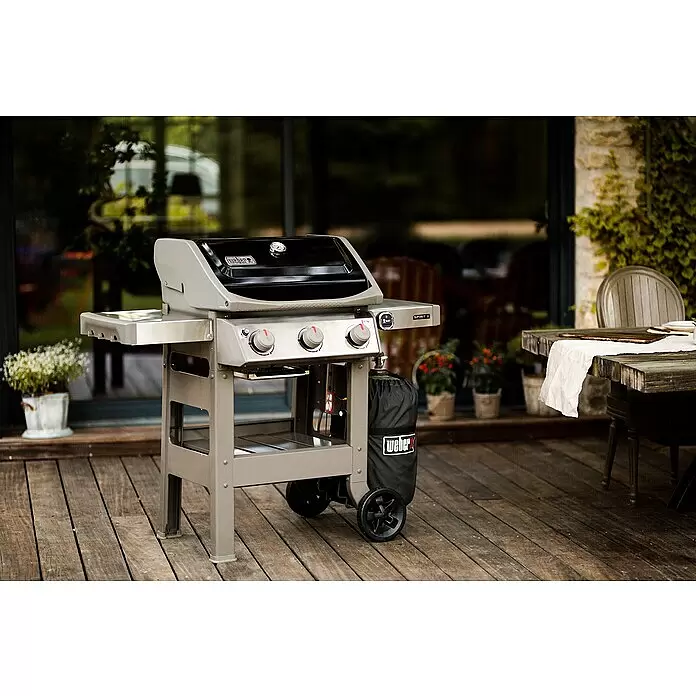 Weber Barbacoa de gas Spirit II E-310 + 7 accesorios - Superficie de la parrilla (An x Pr): 60 x 46 cm, 8,7 kW, Número de quemadores: 3 - Una parrilla de gas Weber Spirit II gris y negra en una terraza de madera, lista para cocinar al aire libre. Tiene tres mandos y estantes laterales.