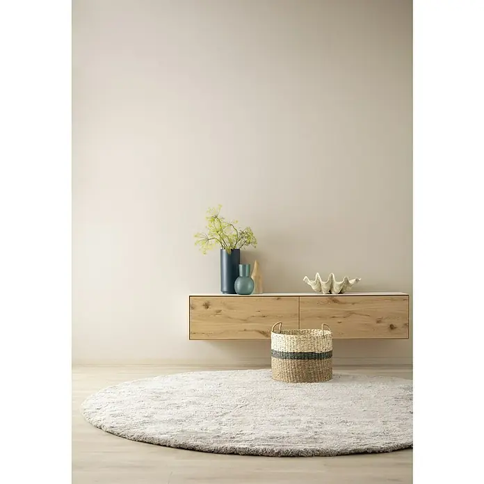 SCHÖNER WOHNEN-Farbe Wandfarbe Designfarbe - Weiches Strandbeige, Matt, 2,5 l, Konservierungsmittelfrei - Schickes Wohnzimmer-Setup mit einem hellen Holzschrank, einer stilvollen Vase und einem runden Teppich, das eine moderne und gemütliche Atmosphäre schafft.