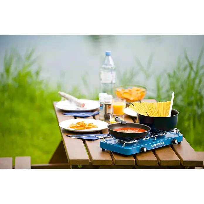 Campingaz Hornillo de gas Base Camp Lid - 43 x 21 x 8,5 cm, 1,6 W - Una cocina Campingaz azul con ollas e ingredientes sobre una mesa de madera, lista para una deliciosa comida al aire libre.