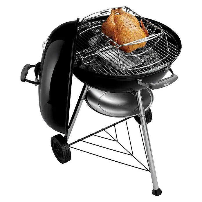 Weber Barbacoa redonda con tapa Compact Kettle - Diámetro de la superficie de la parrilla: 47 cm, Negro - La imagen muestra una parrilla de carbón Weber con un pollo entero cocinándose en ella. La parrilla es negra con una estructura plateada.