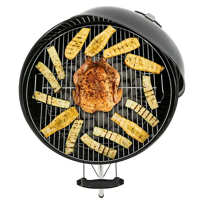 Weber Kugelgrill Original Kettle E-5710 - Durchmesser Grillfläche: 54 cm, Schwarz/Silber - Ein runder Holzkohlegrill mit einem ganzen Hähnchen in der Mitte, umgeben von gegrillten Zucchini-Stücken.