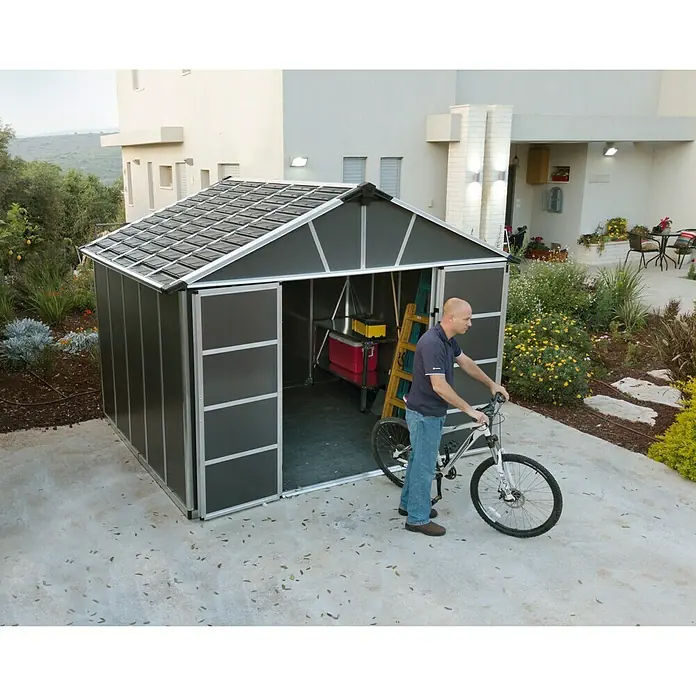 Palram – Canopia Gartenhaus - Außenmaß inkl. Dachüberstand (B x T): 332 x 271 cm, Kunststoff, Grau, Mit Boden - Bild eines modernen Gerätehauses mit Mann und Fahrrad davor, ideal für die Gartenaufbewahrung.