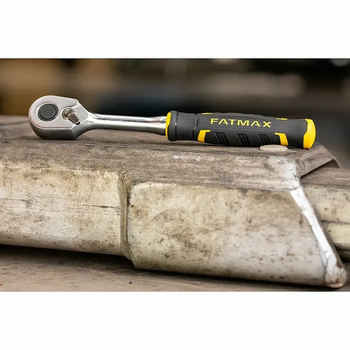 Stanley FatMax Set de llaves de vaso FMMT82680-0 - 22 pzs., Tamaño de accionamiento: ⅜″ - Primer plano de una carraca FATMAX con mango amarillo y negro sobre una superficie metálica sucia.