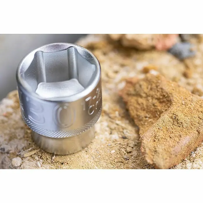 Stanley FatMax Set de llaves de vaso FMMT82680-0 - 22 pzs., Tamaño de accionamiento: ⅜″ - Primer plano de una cabeza de llave de vaso brillante sobre una superficie rugosa junto a un ladrillo, una herramienta utilizada para trabajos de construcción y reparación.