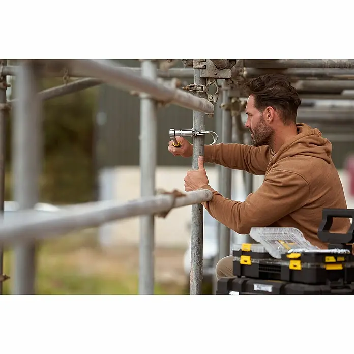 Stanley FatMax Set de llaves de vaso FMMT82680-0 - 22 pzs., Tamaño de accionamiento: ⅜″ - Un hombre asegura un componente a un andamio con herramientas de una caja de herramientas Stanley.