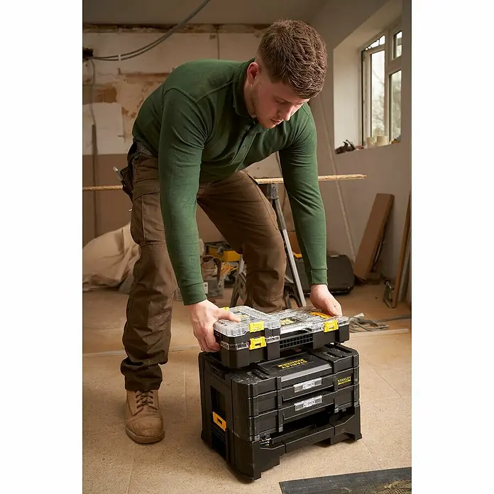 Stanley FatMax Set de llaves de vaso FMMT98101-0 - 48 pzs., Tamaño de accionamiento: ¼″ - Un hombre coloca una caja de herramientas Stanley encima de una pila de otras cajas de herramientas Stanley en una habitación en renovación.