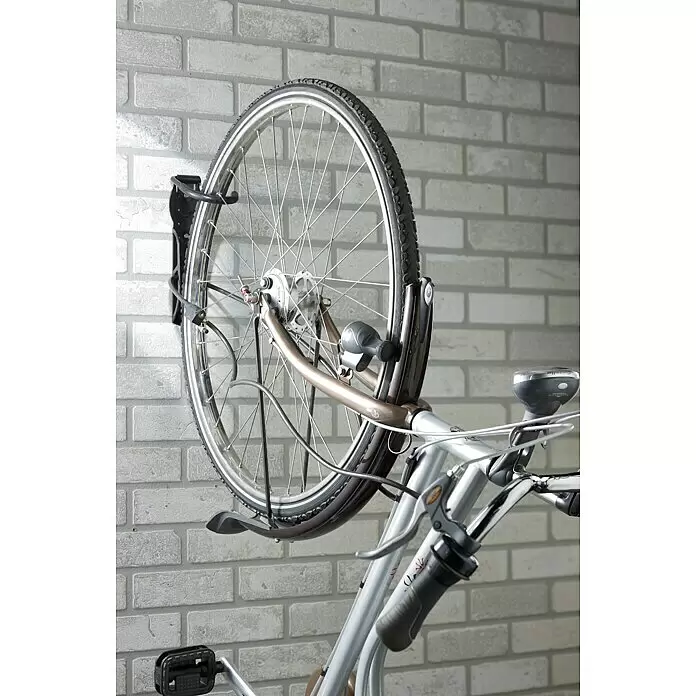 Mottez Gancho de pared para bicicletas B865V - Acero, Negro - Parte delantera de una bicicleta montada verticalmente en un soporte de pared negro contra una pared de ladrillo claro.