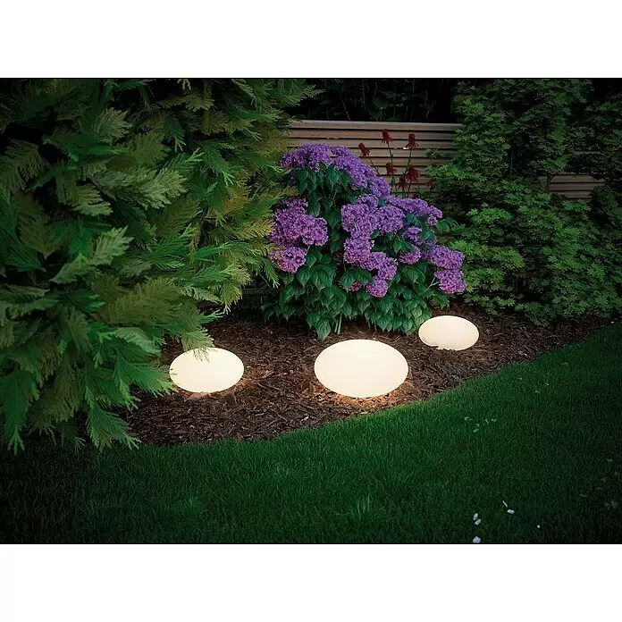 Paulmann Plug & Shine LED-Dekoleuchte Stone - 2,8 W, Weiß, L x B x H: 28 x 28 x 16,6 cm - Drei leuchtende kugelförmige Gartenleuchten erhellen ein Blumenbeet mit lila Blüten und grünem Laub, eingebettet in Rindenmulch neben einem Rasen.