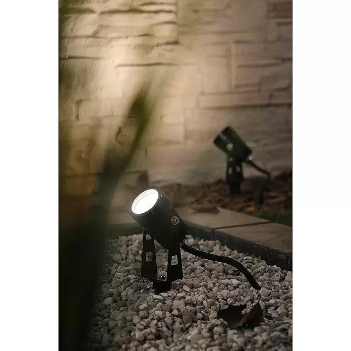 Paulmann Plug & Shine LED-Gartenspot - Erdspieß, Höhe: 26 cm - Zwei schwarze Outdoor-Spots auf Kies beleuchten eine Steinmauer bei Nacht.