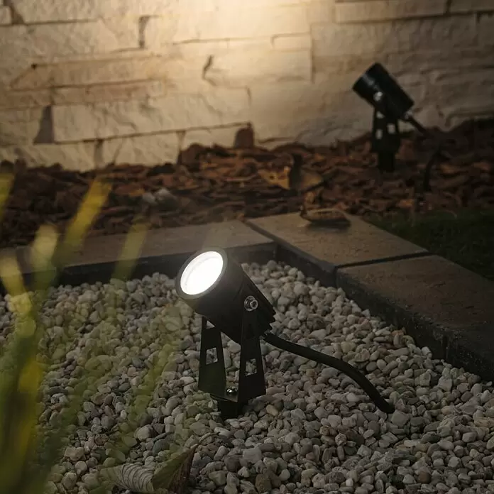 Paulmann Plug & Shine LED-Gartenspot - Erdspieß, Höhe: 26 cm - Schwarzer Außenstrahler beleuchtet eine Steinwand in einer Gartenanlage.