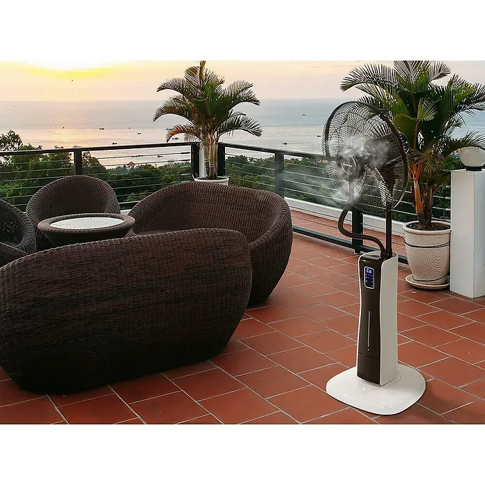Purline Misty Ventilador de pie 2 - Blanco, Altura: 130 cm - Un moderno ventilador de pedestal blanco con función de nebulización en una terraza con vistas al mar, que proporciona un enfriamiento refrescante.
