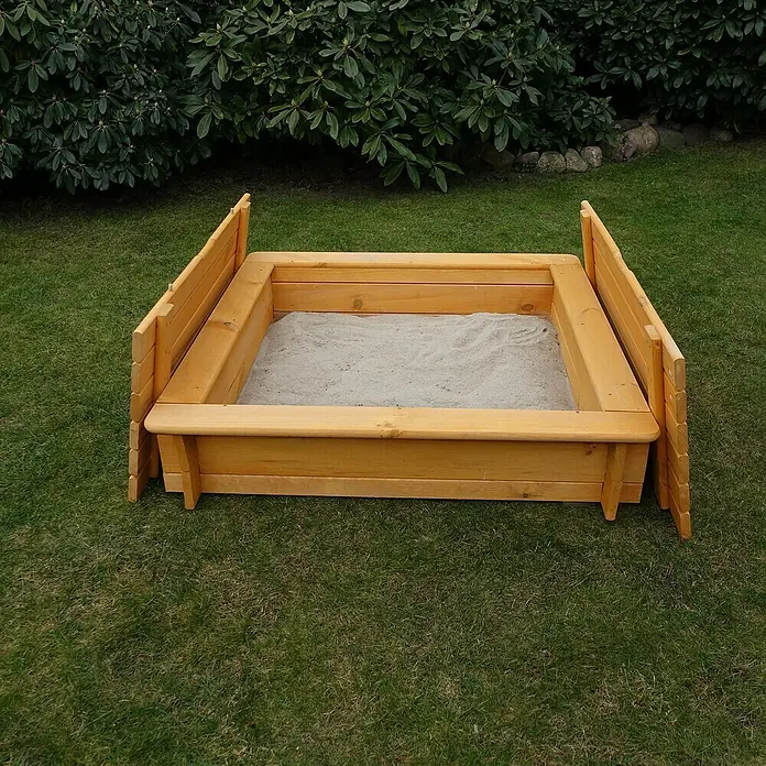Promadino Sandkasten Tessa100 x 100 x 24 cm, Kiefer - Ein hölzerner Sandkasten mit hochklappbaren Seitenwänden steht auf einem Rasen im Garten. Er ist mit Sand gefüllt und bereit zum Spielen.