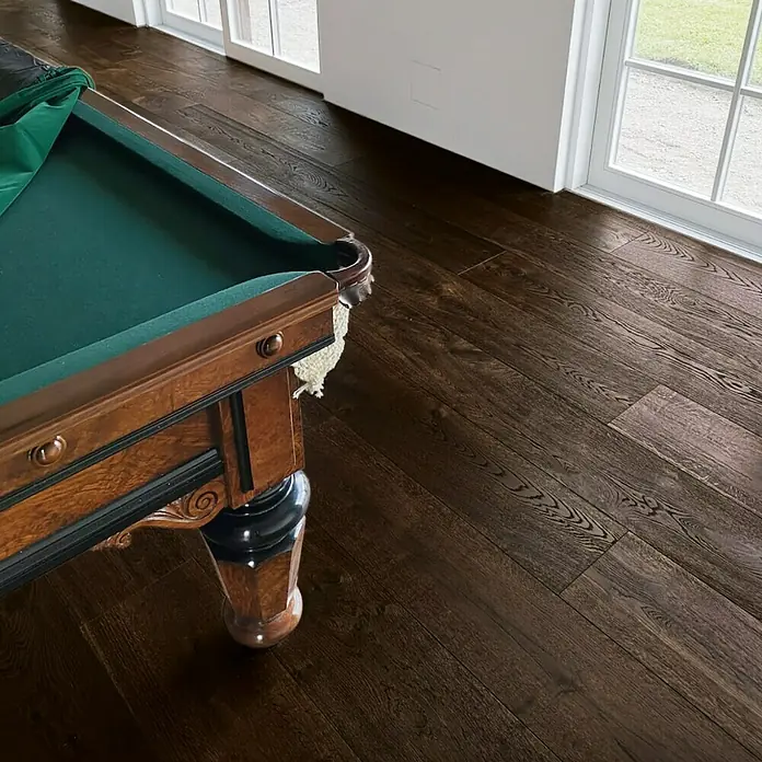 Parkettmuster Eiche Julia - 280 x 160 x 15 mm, Landhausdiele - Nahaufnahme eines Billardtisches mit grünem Tuch und Holzakzenten, der auf einem dunklen Holzboden steht. Perfekt für ein Spielzimmer.