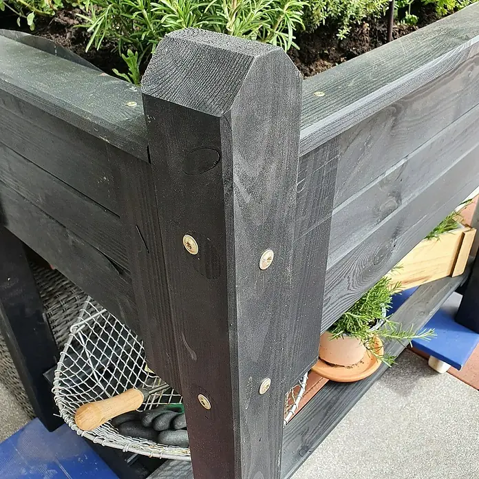 Promadino Kräuterhochbeet - L x B x H: 90 x 60 x 84,5 cm, Anthrazit - Nahaufnahme eines stilvollen, erhöhten Gartenbeets aus dunklem Holz mit markanten Schrauben und üppigem Grün.