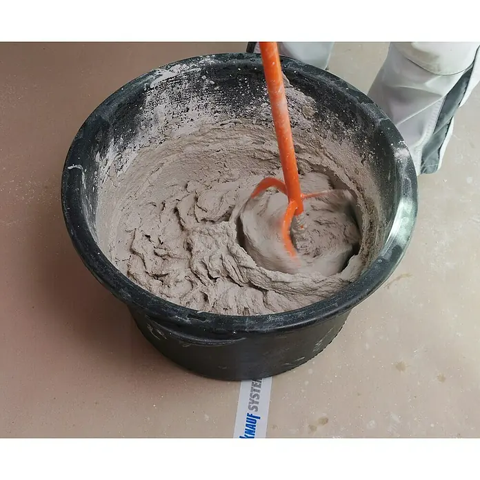 Knauf Rotband Haftputzgips - 30 kg - Mörtel wird mit einem orangefarbenen Rührer in einem schwarzen Eimer gemischt, um eine gleichmäßige Konsistenz zu erzielen.