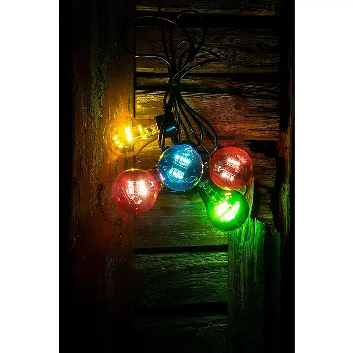 Konstsmide LED-Lichterkette - Außen, Lichtfarbe: Mehrfarbig, Batteriebetrieben - Bunte Lichterkette mit fünf farbigen Glühbirnen (gelb, blau, rot, grün) an einer rustikalen Holzwand, die farbige Lichter wirft.