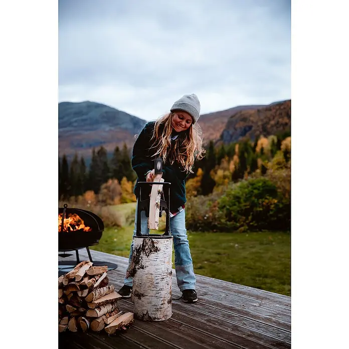 Kindling Cracker Holzspalter KingMax. Spaltgutdurchmesser: 22 cm - Ein junges Mädchen spaltet mit einem Holzspalter Holz, während im Hintergrund ein Lagerfeuer brennt, perfekt für gemütliche Outdoor-Momente.