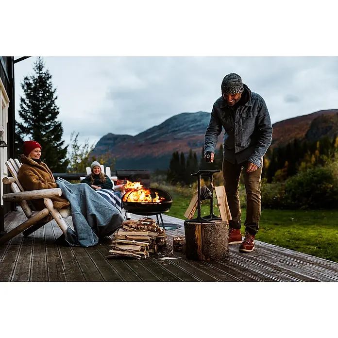 Kindling Cracker Holzspalter King - Max. Spaltgutdurchmesser: 22 cm - Ein Mann spaltet Holz mit einem Holzspalter, während zwei Frauen sich am Feuer entspannen. Der Holzspalter steht im Fokus.