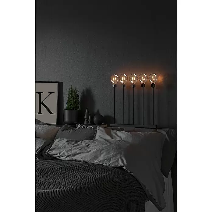 Konstsmide LED-Dekoleuchte - 3,5 W, L x B x H: 45 x 13 x 50 cm - Fünfflammige schwarze Metall-Nachttischlampe mit warm leuchtenden Glühbirnen in einem dunklen Schlafzimmer.