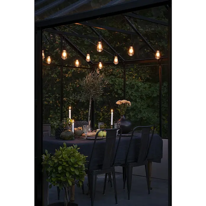 Konstsmide LED-Lichterkette Globe - Außen, Lichtfarbe: Bernstein, Netzbetrieben, Oval - Stimmungsvolles Ambiente mit Edison-Glühbirnen, die ein elegantes Abendessen in einem Gewächshaus beleuchten. Kerzen und Blumen auf dem Tisch.