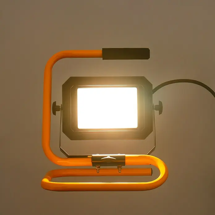 Profi Depot LED-Strahler - 30 W, 4.950 lm, 4.000 K, L x B x H: 22,9 x 29 x 35,4 cm, IP65 - Nahaufnahme einer Arbeitsleuchte mit orangefarbenem Rahmen und hellem Lichtschein. Die Leuchte steht stabil und bietet gute Ausleuchtung.
