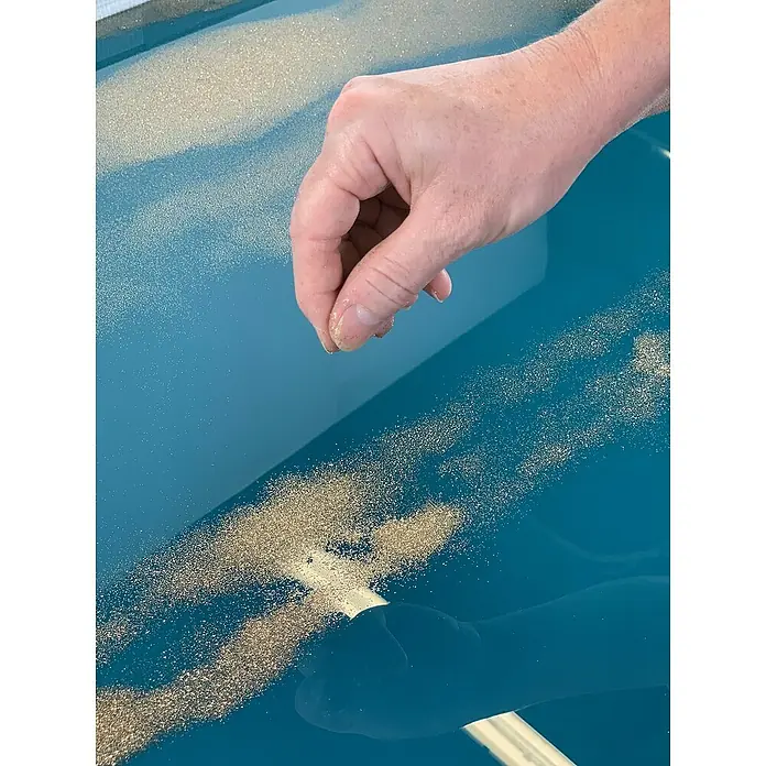 Fleur Purpurina Glitter - Dorado, 90 g, Brillante - Mano esparciendo purpurina dorada sobre una superficie azul brillante. Elementos decorativos para proyectos de arte.