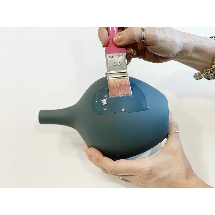 Fleur Barniz - Transparente brillante, 130 ml - Primer plano de un decantador gris que está siendo tratado con un pincel y pintura.